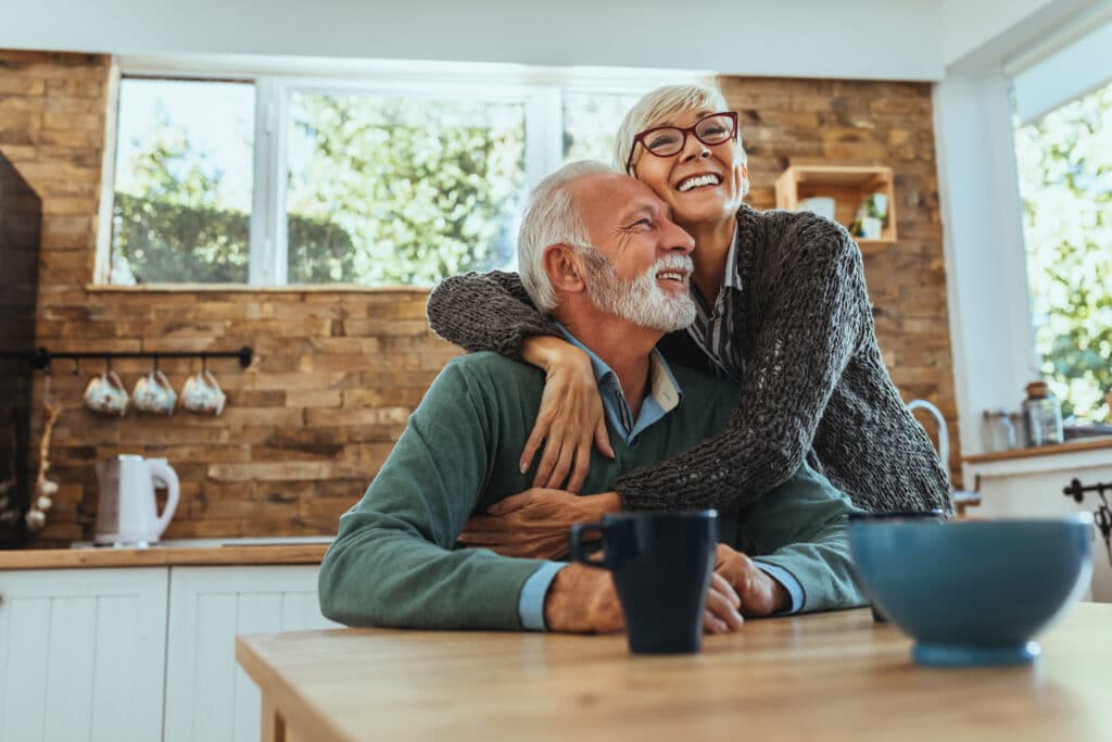 An elderly couple sharing a joyful embrace at home.