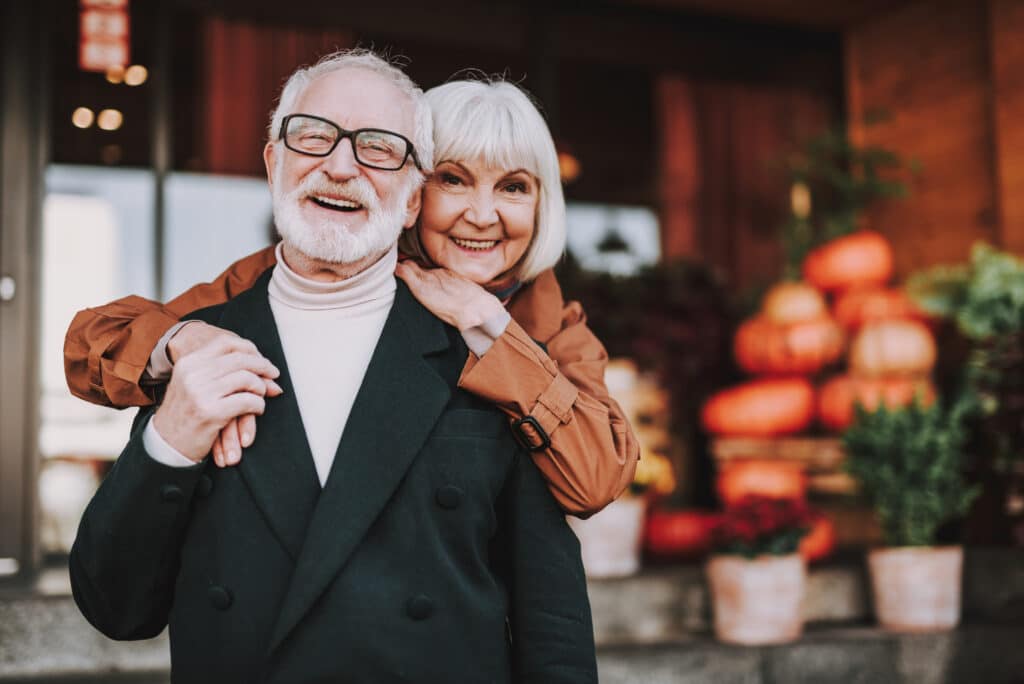 Elderly couple smiling warmly outdoors with blurred background.