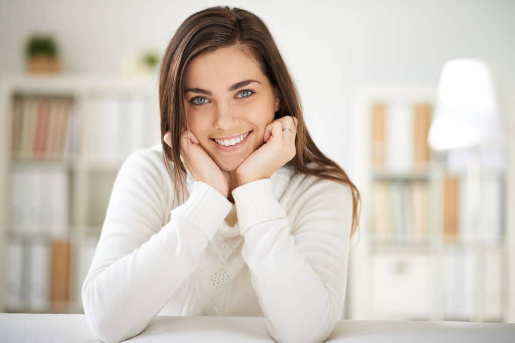Smiling woman resting her chin on her hands, looking at the camera.
