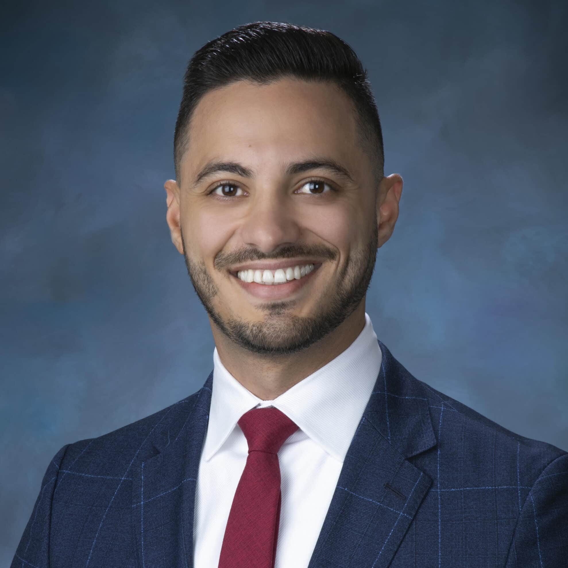 Professional man in suit smiling against a blue background.
