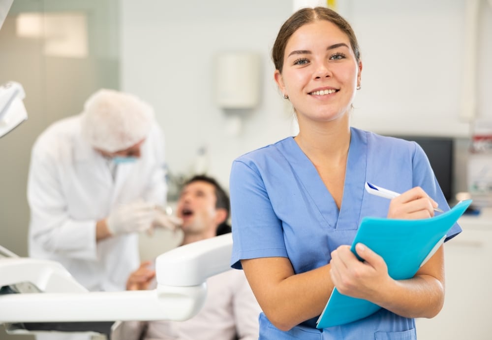 A smiling dental hygienist holding a clipboard in a clinic.