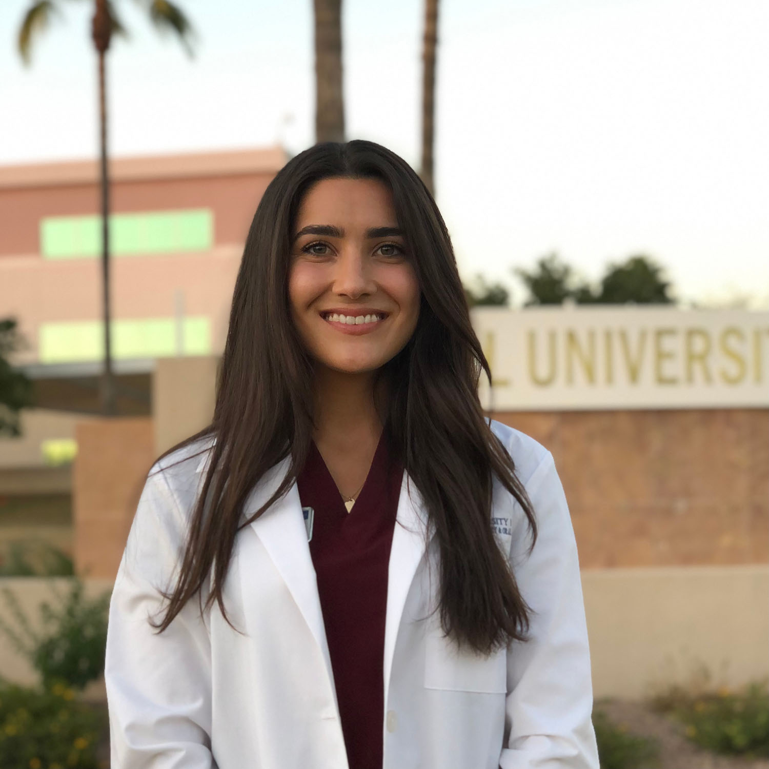 Young woman in a white coat smiling outdoors at a university campus.